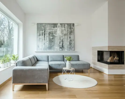 wohnen-einrichten-wohnzimmer-einrichtung-moebel-kamin-01 Geräumiges weißes Wohnzimmer mit grauer Eckcouch, großem modernem Gemälde und Kamin.